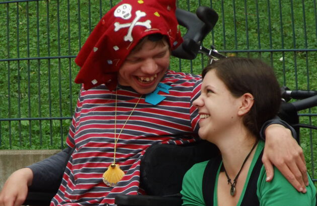 Foto einer Person im Rollstuhl die Spaß hat und eine Frau anlächelt.