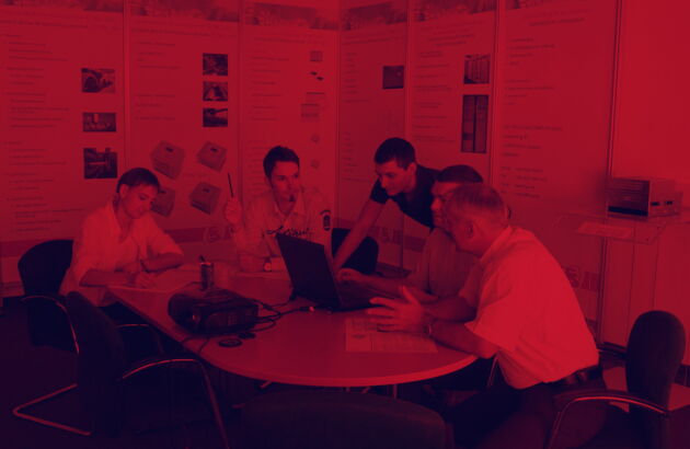 Rötliches Bild - Fünf Personen sitzen einem Tisch und beraten sich.